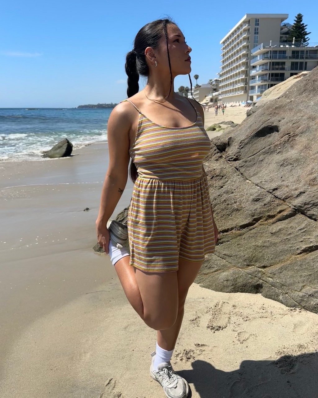 Woman in a striped dress standing on a beach with buildings in the background