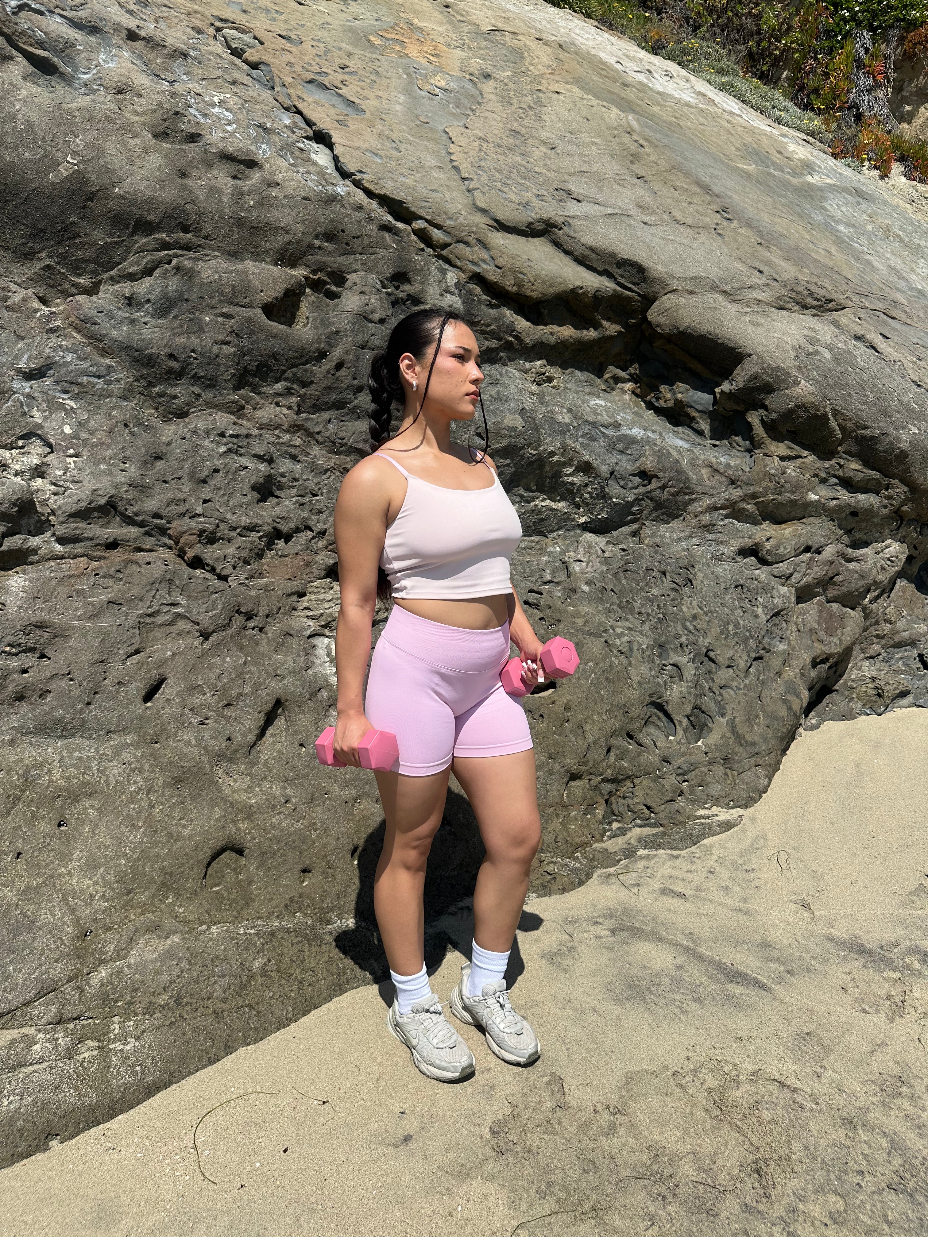 Woman exercising with pink dumbbells against a rocky background