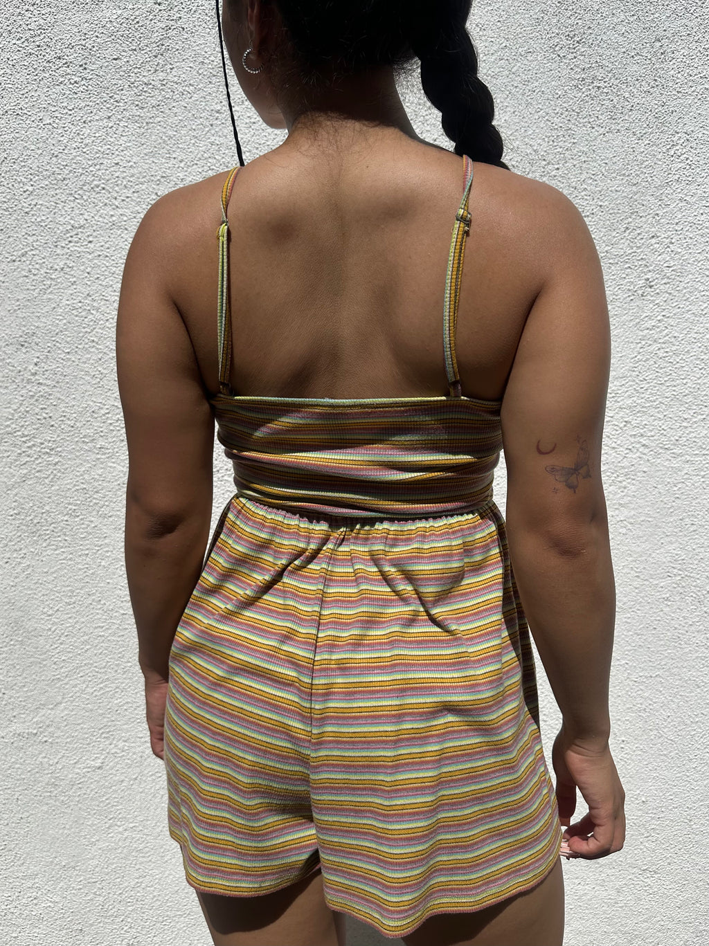 A women wearing a striped tank top and shorts against a light gray wall