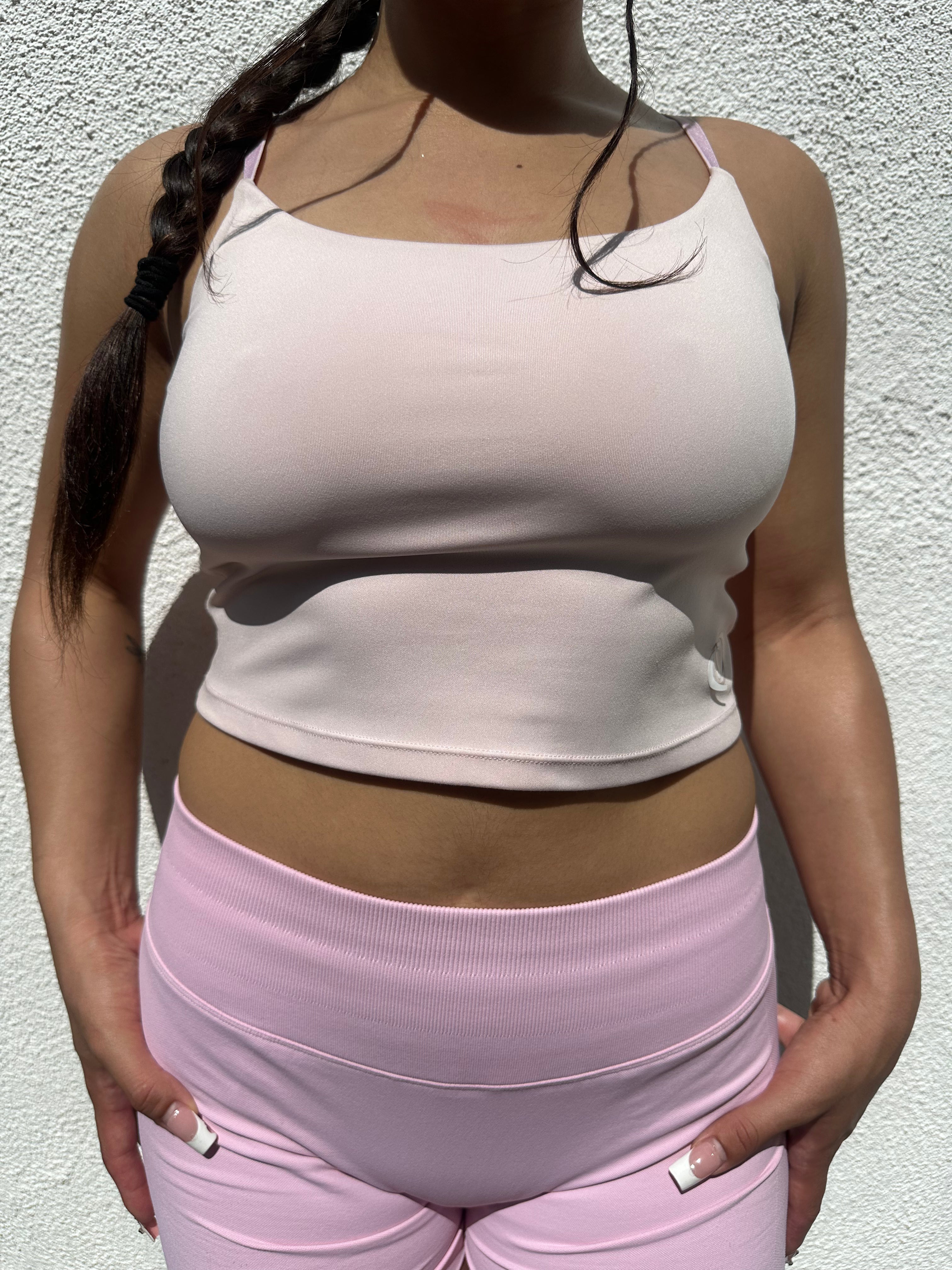 Person wearing a light pink tank top and pants against a neutral background